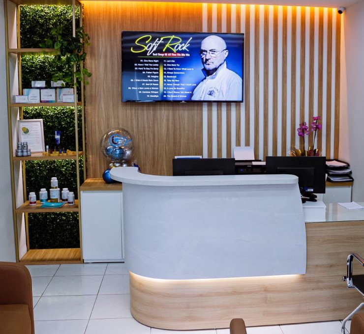 Sala de espera de clínica com móveis planejados, painel ripado e balcão de recepção projetado em L curvo, branco e amadeirado em São Luís, Maranhão.